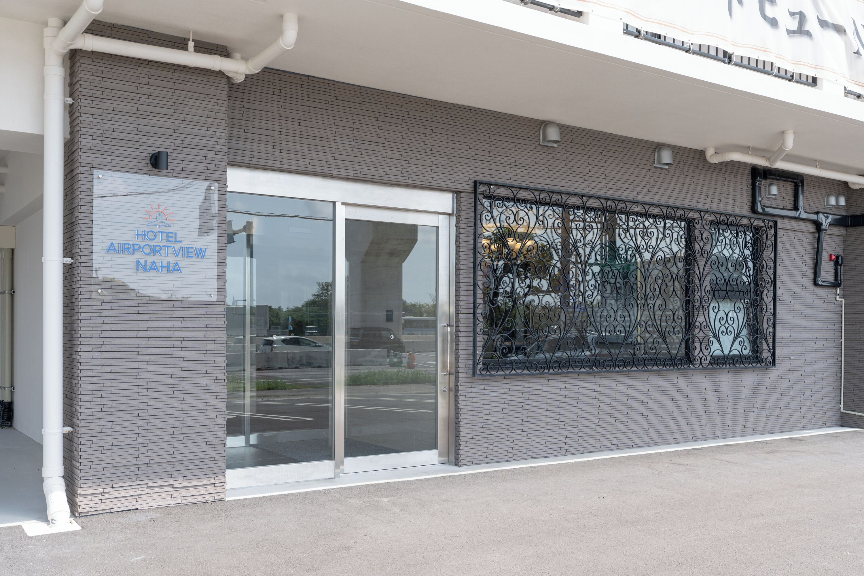 A modern building with a glass entrance, a sign reading "HOTEL AIRPORTVIEW NAHA," and a decorative metal gate.