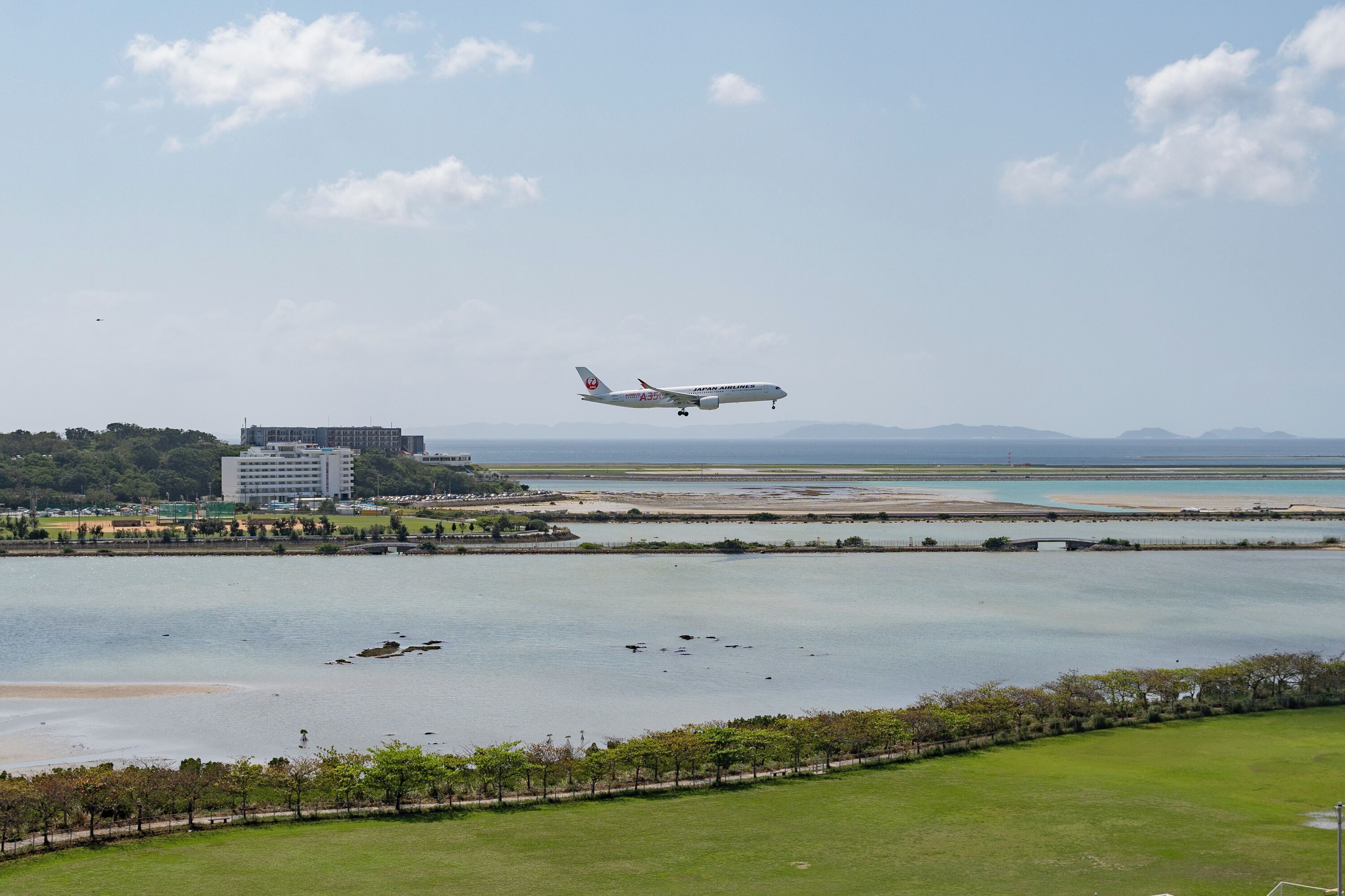 An airplane landing at an airport near a body of water with a bridge in the background.