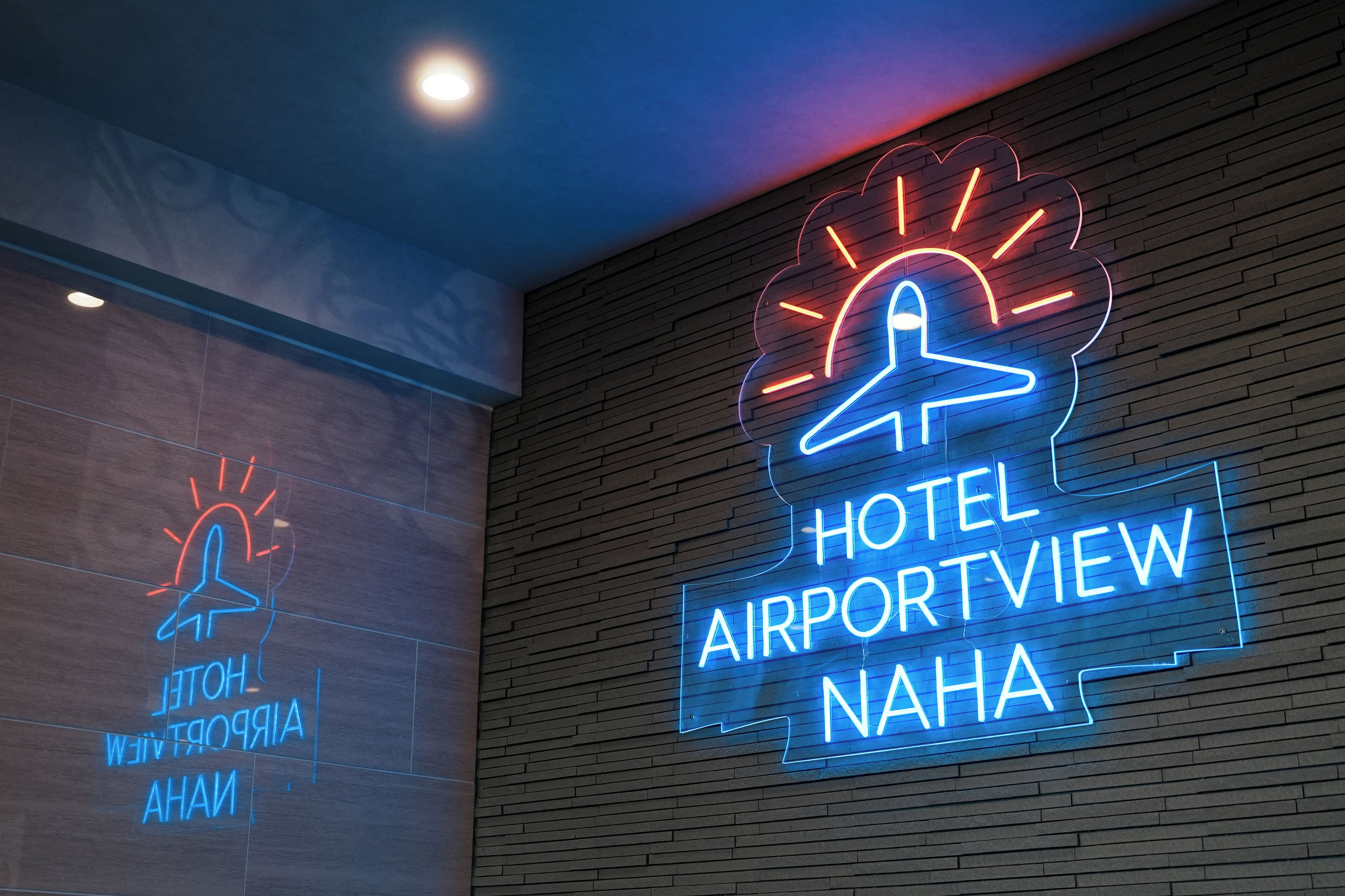 Ein Neon-Schild des Hotels HOTEL AIRPORTVIEW NAHA mit einem stilisierten Flugzeug- und Sonnendesign.