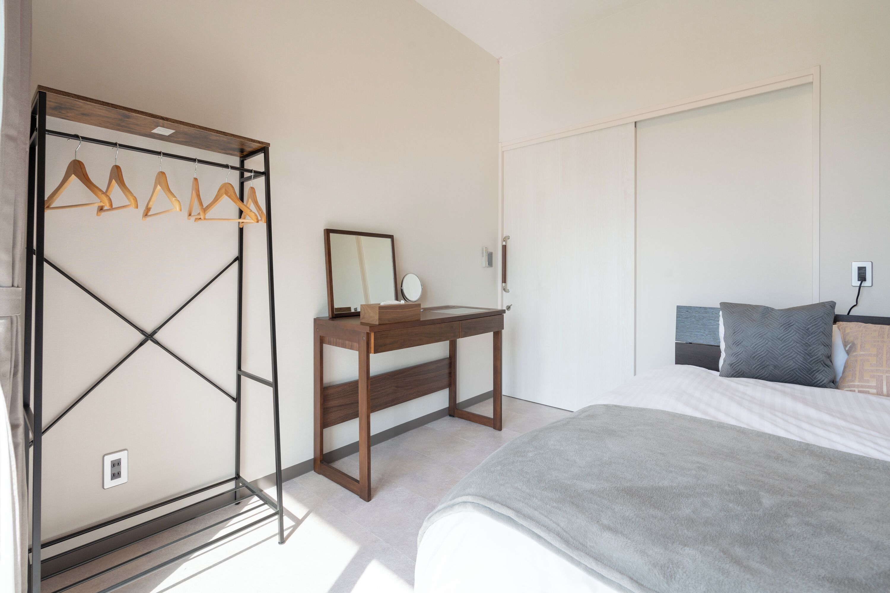 Un dormitorio con cama, escritorio de madera, espejo y perchero.