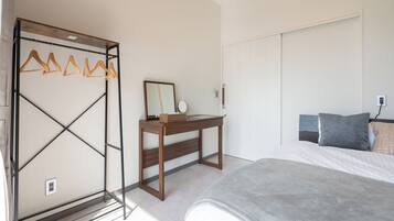 Un dormitorio con cama, escritorio de madera, espejo y perchero.