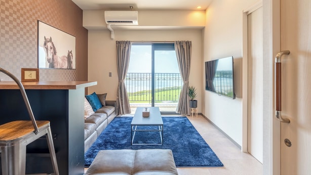 Un salon moderne avec un canapé, une table basse et un téléviseur. Il y a un balcon avec vue sur l’extérieur.