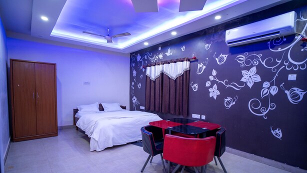 A bedroom with a bed, a wardrobe, a table with chairs, and a wall with floral designs. - Hotel Atithi Bhawan (Golmuri)