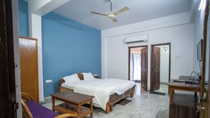 A bedroom with a bed, a wooden table, a chair, and a ceiling fan. - Hotel Atithi Bhawan (Golmuri)