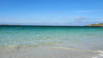 Une plage à l’eau turquoise et limpide, un rivage sablonneux et un phare qui se dresse au loin.