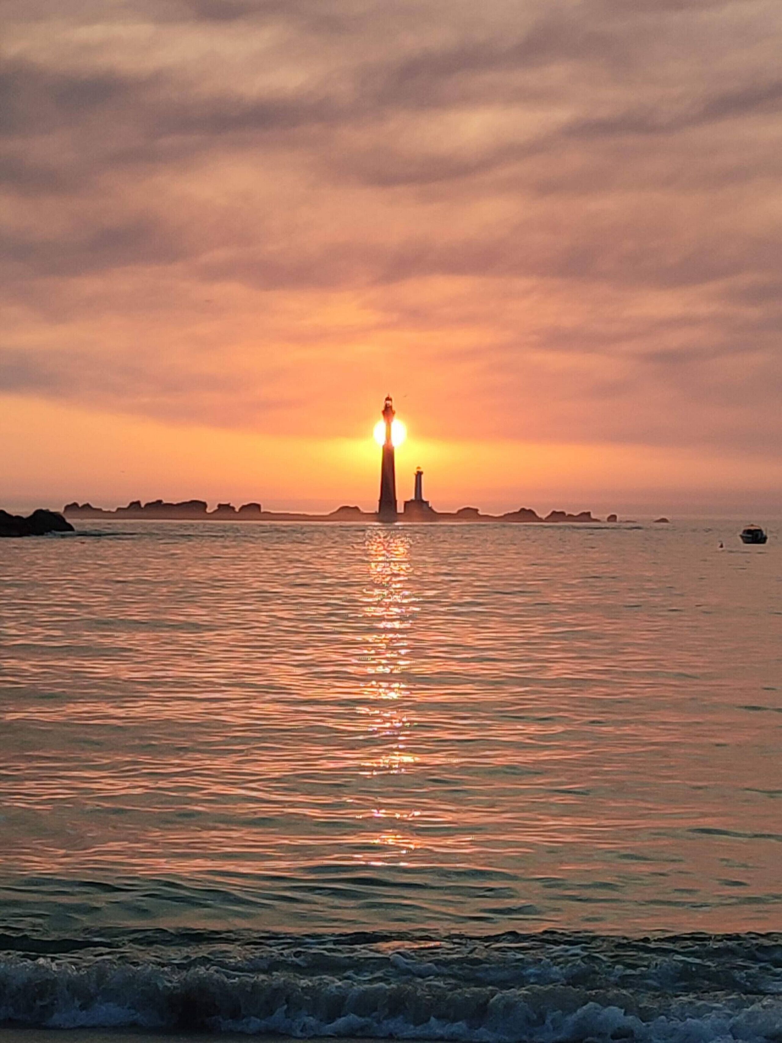 A coastal scene with a lighthouse and calm sea during sunset.