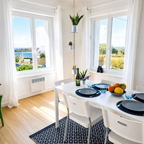 A dining area with a table set for two, a view of the sea, and a hanging plant.
