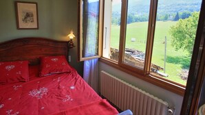 Quarto com cabeceira de madeira, colcha vermelha e vista para uma paisagem verde pela janela.