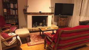 Uma sala de estar acolhedora com lareira, estante de livros, televisão e assentos confortáveis.