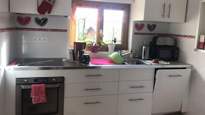 Eine Küche mit weißen Schränken, einem Herd, einer Mikrowelle und einem Fenster mit Pflanzen.