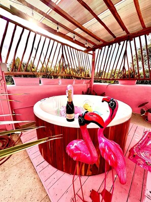 A pink-themed outdoor area with a hot tub, a flamingo sculpture, and a bottle of champagne.