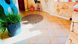 A spacious room with a stone wall, a circular woven rug, and several potted plants.