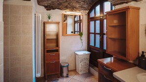A bathroom with a rustic stone ceiling, a wooden cabinet, a radiator, a sink, and a trash bin. - Alpine home with panoramic terrace and fireplace (Villaretto)