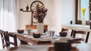 A dining table with a vase of flowers, bowls of fruit, and a rustic wooden chair. - Alpine home with panoramic terrace and fireplace (Villaretto)