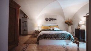 A bedroom with a sloped ceiling, a bed with a patterned bedspread, a nightstand with a lamp, a vase with flowers, and a wall-mounted phone. - Alpine home with panoramic terrace and fireplace (Villaretto)