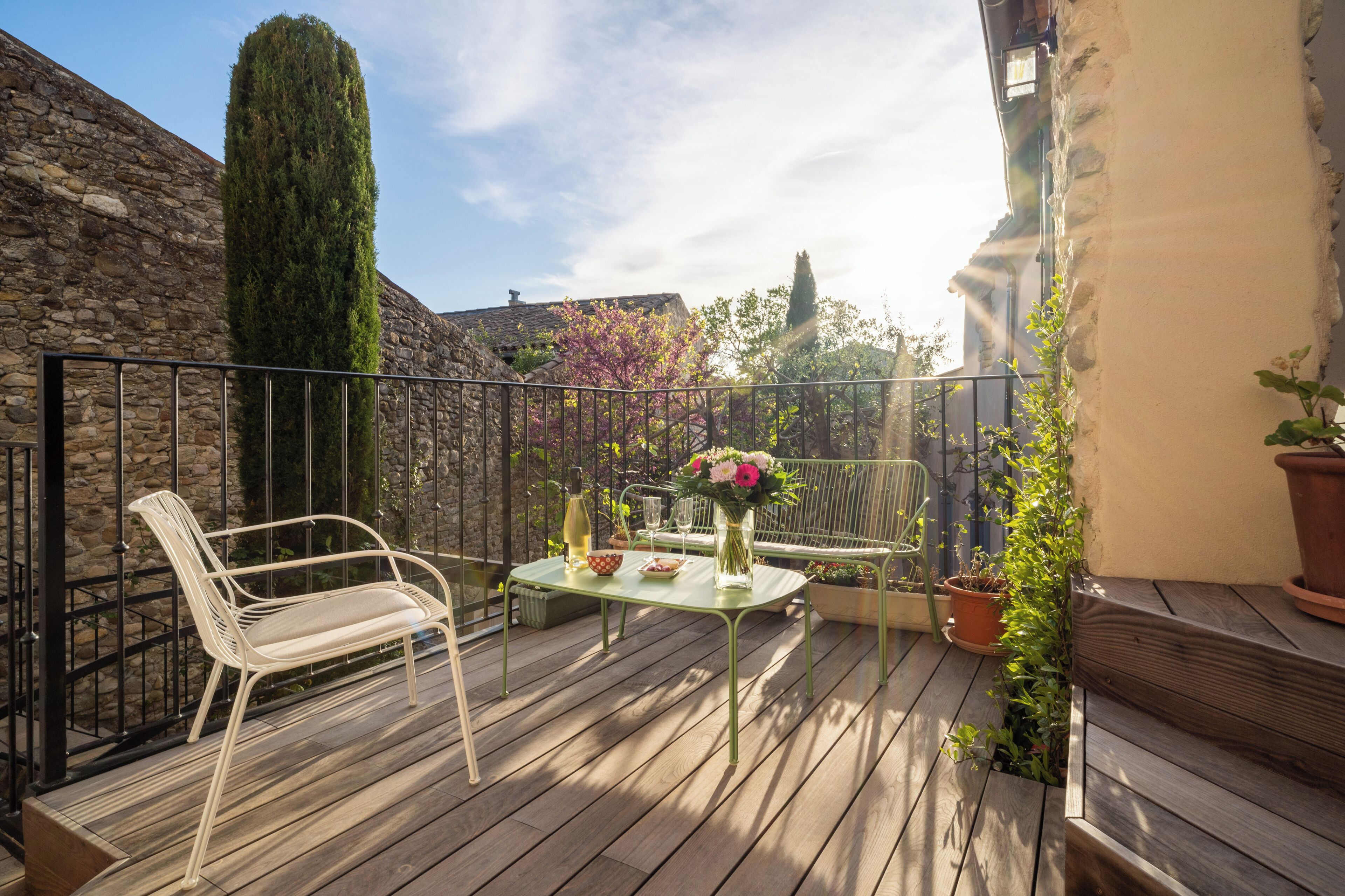 A wooden deck with a table and chairs, surrounded by stone walls and potted plants.