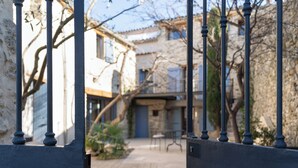 A courtyard with a stone pathway, a gate with black metal bars, and a building with a blue door.