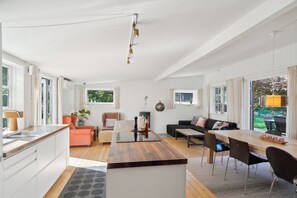 Eine moderne Küche mit einer Holzinsel, einem Essbereich mit langem Tisch und Stühlen, einem Sofa und Blick auf den Garten.