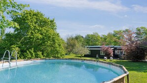 A clear swimming pool with a wooden deck, surrounded by lush greenery and a house in the background. - Spacious summer house with pool. (Vejby)