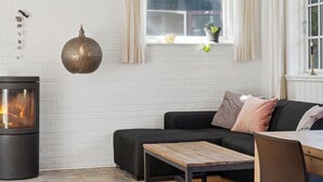 A modern living room with a fireplace, a sofa, a coffee table, and a window with curtains. - Spacious summer house with pool. (Vejby)