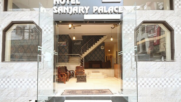 La entrada del Hotel Sanjay Palace con un patrón de suelo a cuadros, una escalera y una zona de estar con muebles de madera.