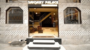 La entrada al Hotel Sanjay Palace con fachada de mármol a cuadros, una escalera que conduce al interior y un cartel sobre la entrada.