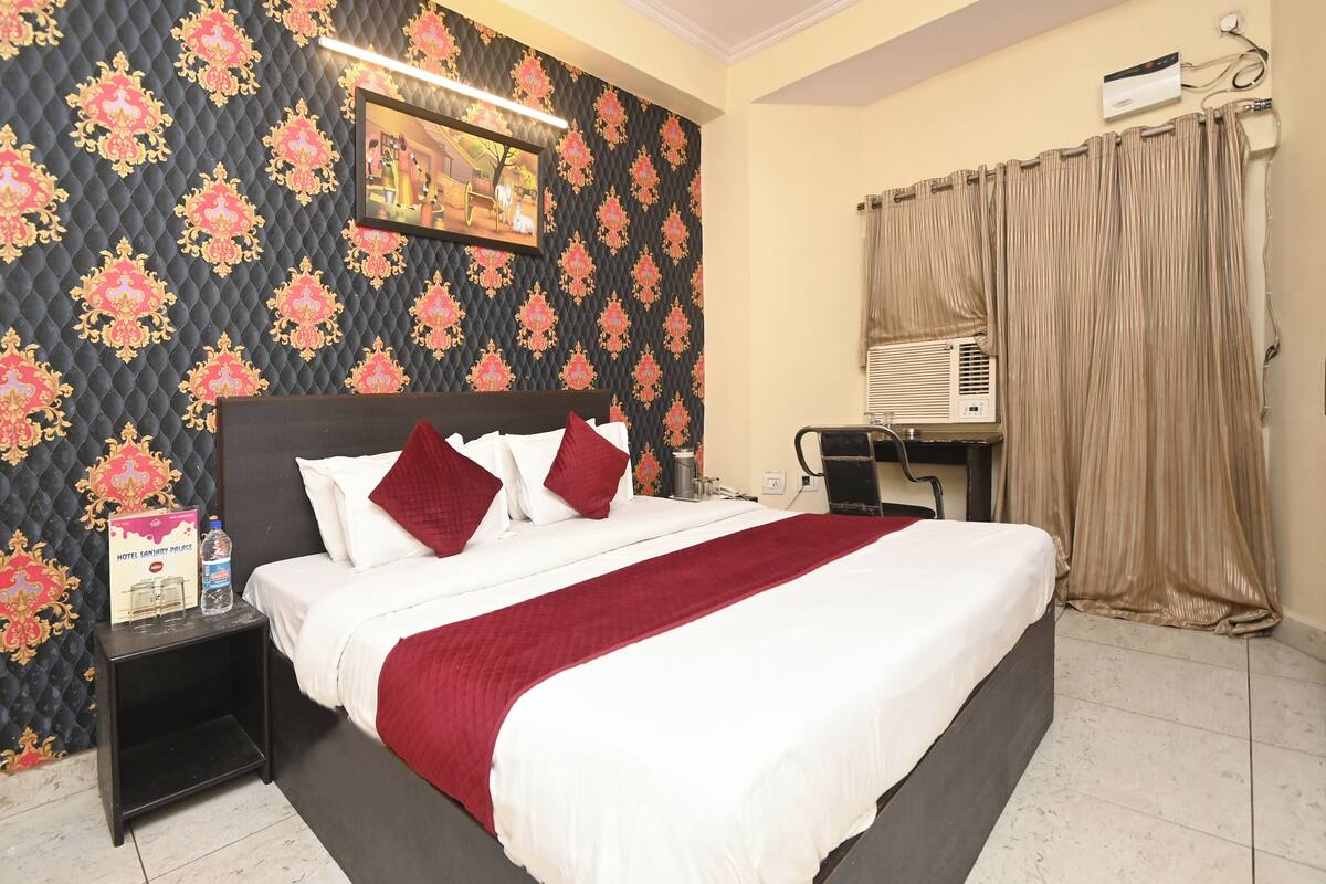 Una habitación de hotel con cama, mesita de noche, aire acondicionado de pared y cortina.