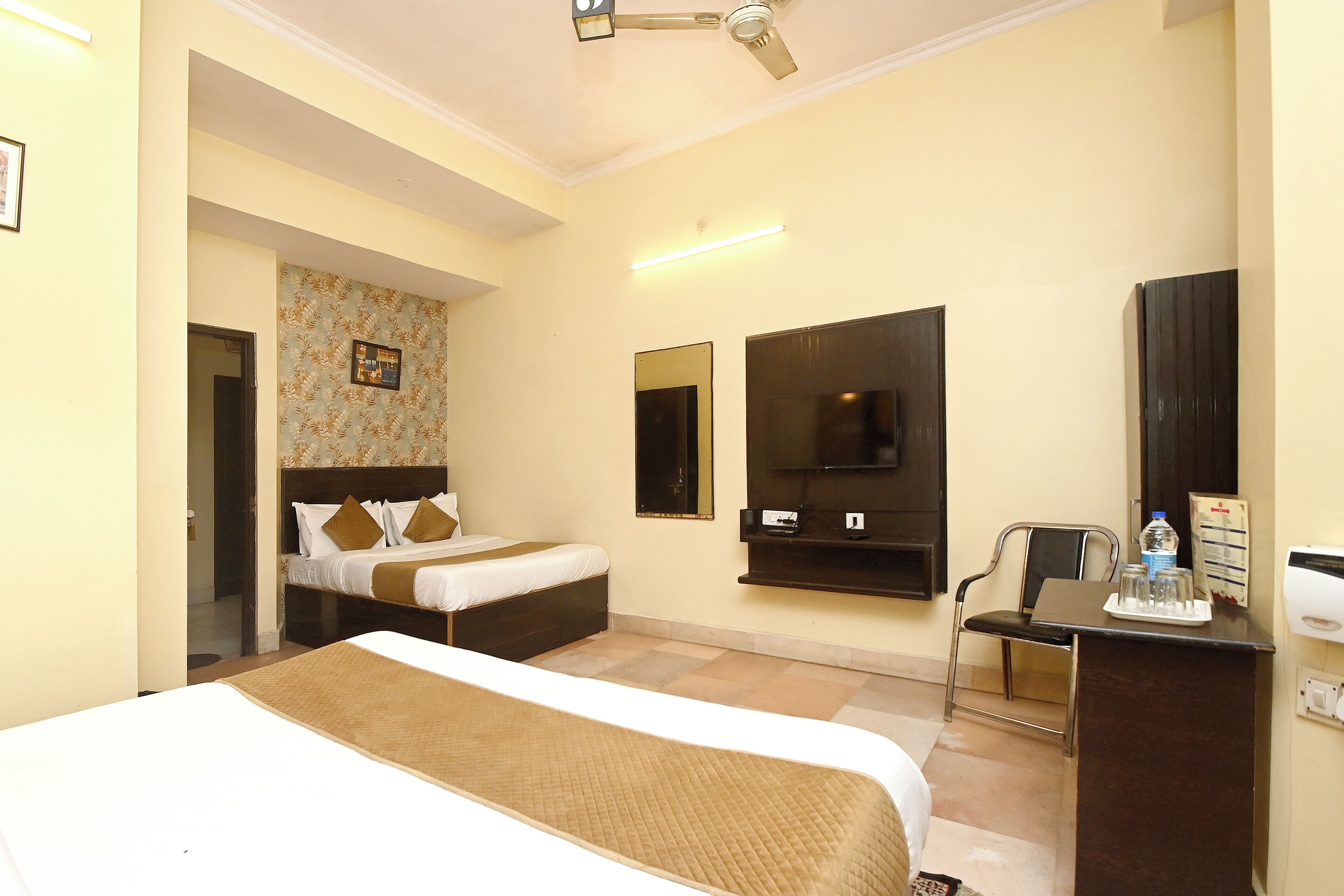 A hotel room with two beds, a desk, a chair, a TV, and a mirror.