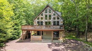 A two-story stone cabin with a balcony, surrounded by dense forest.