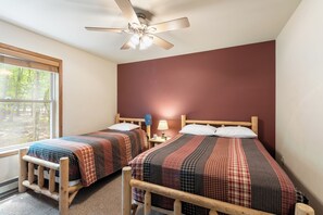 Ein Schlafzimmer mit zwei hölzernen Betten, einem Deckenventilator, einem Fenster und einem Nachttisch mit Lampe.