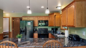 A kitchen with wooden cabinets, granite countertops, a refrigerator, stove, microwave, and a toaster.