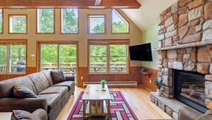 A spacious living room with a stone fireplace, large windows, and a ceiling fan.