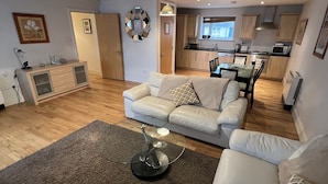 A modern living room with a sofa, a coffee table, and a kitchen in the background. - 17 Shearwater overlooking Kinsale Harbour (Kinsale)