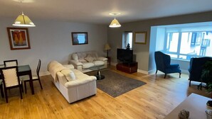 A living room with a sofa, armchair, TV, and dining area. - 17 Shearwater overlooking Kinsale Harbour (Kinsale)