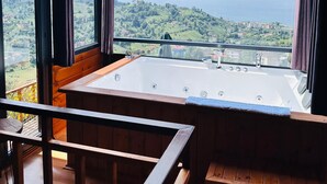 Une chambre dotée d’une grande baignoire, de poutres en bois et offrant une vue sur un paysage verdoyant et la mer.
