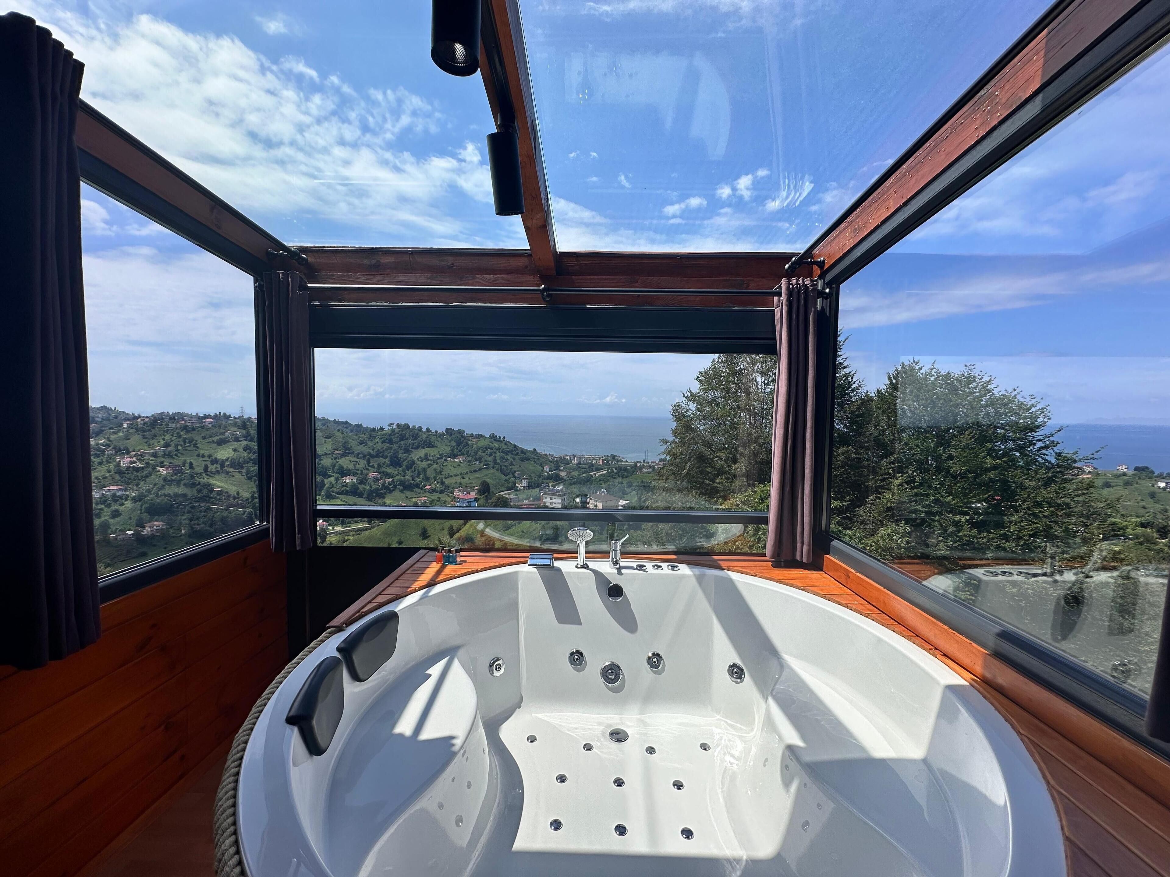 A modern bathroom with a large bathtub, wooden walls, and a view of a coastal landscape.