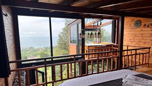 Une cabane en bois dotée d’une grande fenêtre donnant sur la mer et la verdure.