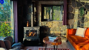 L’intérieur d’un chalet accueillant, avec un mur en pierre, un poêle à bois, un canapé et un tapis à motifs.