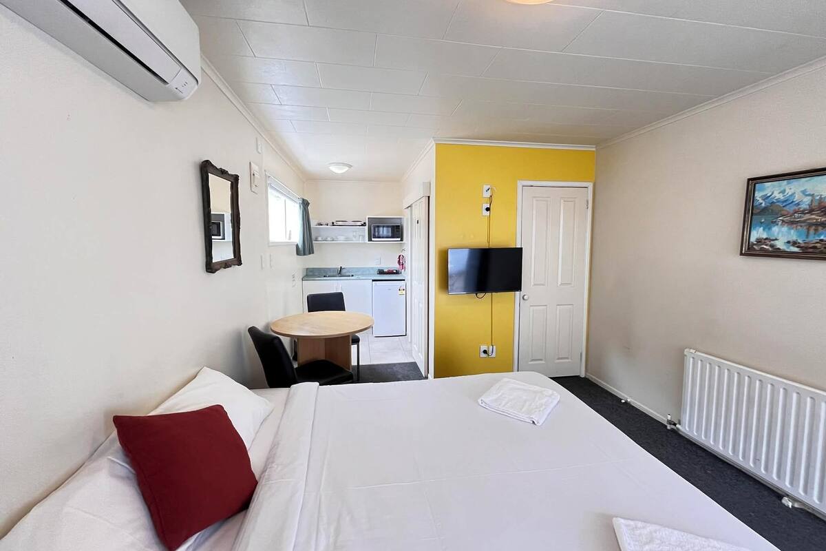 A hotel room with a bed, a small table, a microwave, a TV, and a painting on the wall.