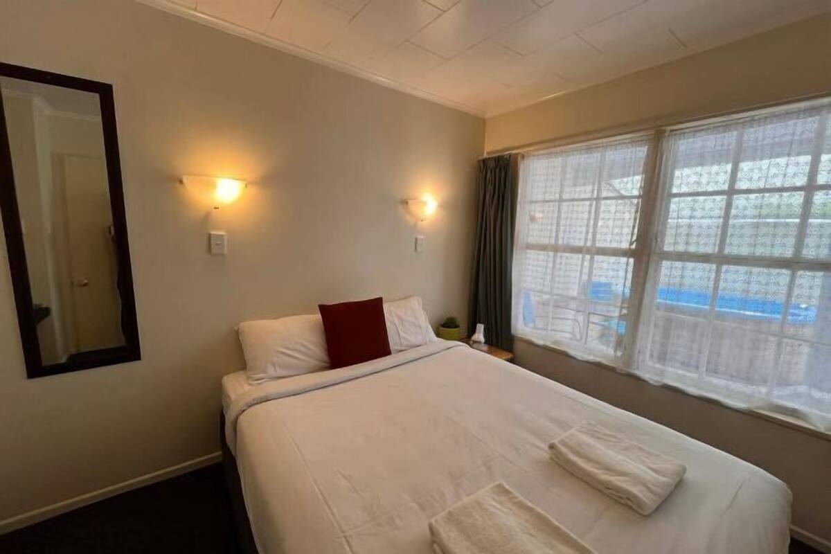 A hotel room with a bed, a mirror, two wall-mounted lights, and a window with a view.