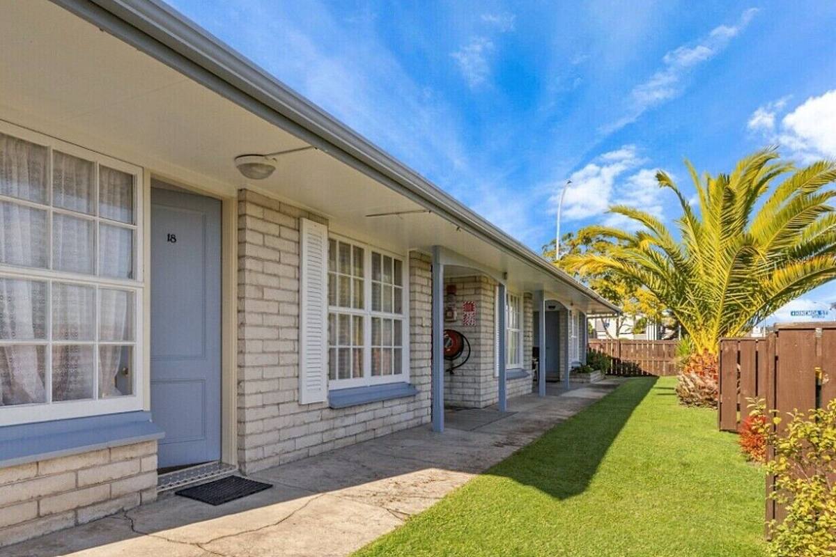 A single-story building with a covered porch, a well-maintained lawn, and a palm tree.