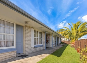 A single-story building with a covered porch, a well-maintained lawn, and a palm tree. - Kowhai motel (Rotorua)