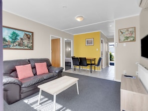 A living room with a sofa, coffee table, and a dining area with chairs and a table. - Kowhai motel (Rotorua)