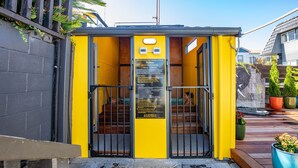 A yellow entrance gate with a notice board, a staircase leading to a building, and potted plants. - Kowhai motel (Rotorua)