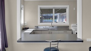 A modern kitchen with a bar counter, a window with a view of the outside, and a built-in oven. - Kowhai motel (Rotorua)