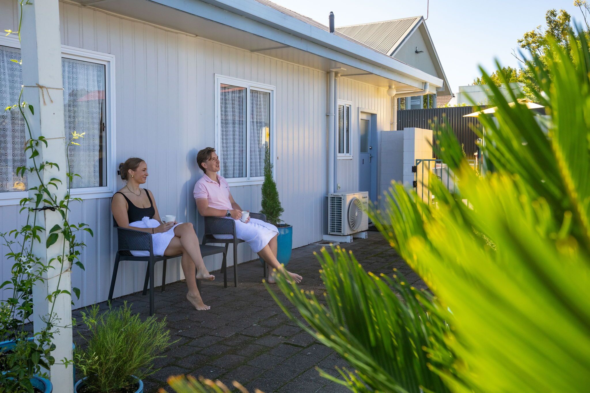 Two people seated on a porch with a house in the background.