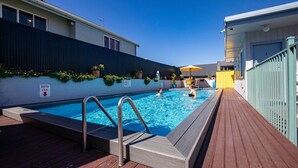 A swimming pool with a wooden deck, a metal ladder, and a depth marker. - Kowhai motel (Rotorua)