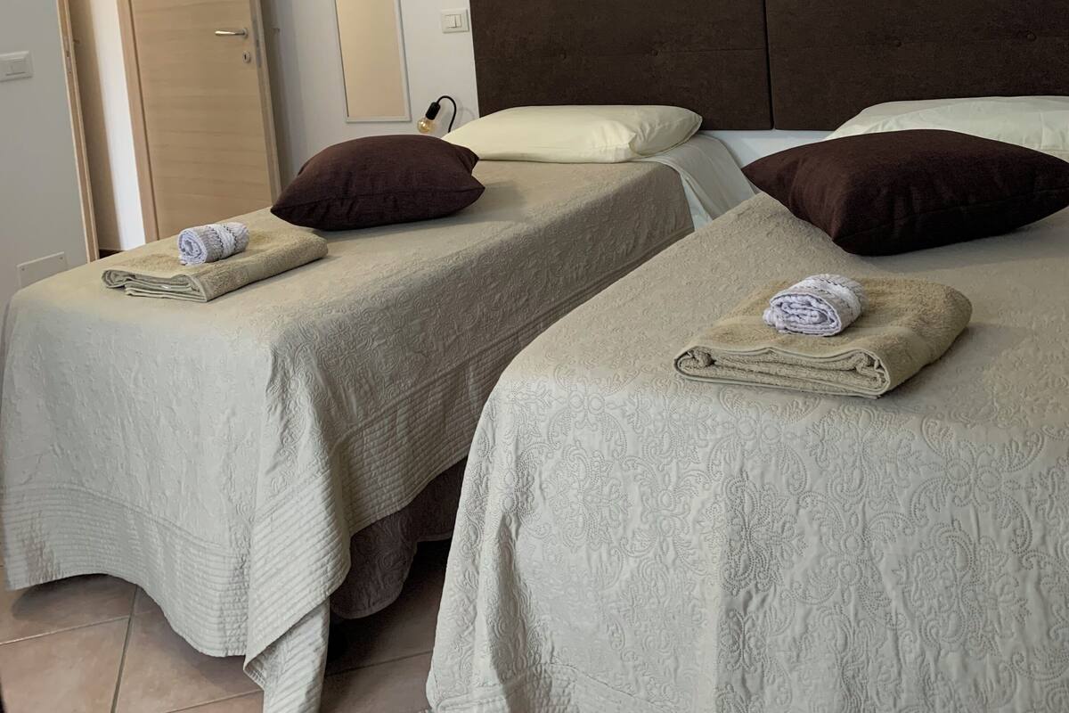 Une chambre d’hôtel avec deux lits, chacun agrémenté d’une serviette roulée et de plusieurs oreillers. Trois tableaux représentant des motifs floraux sont accrochés au mur.