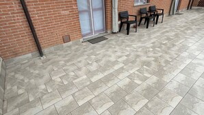A covered outdoor area with tiled flooring, a brick wall, and a row of chairs. - Quadrifoglio affittacamere (Novi Ligure)