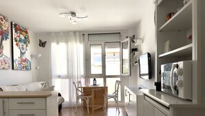 Eine moderne Küche mit weißen Schränken, ein Essbereich mit Holztisch und -stühlen sowie ein großes Fenster mit Vorhängen.